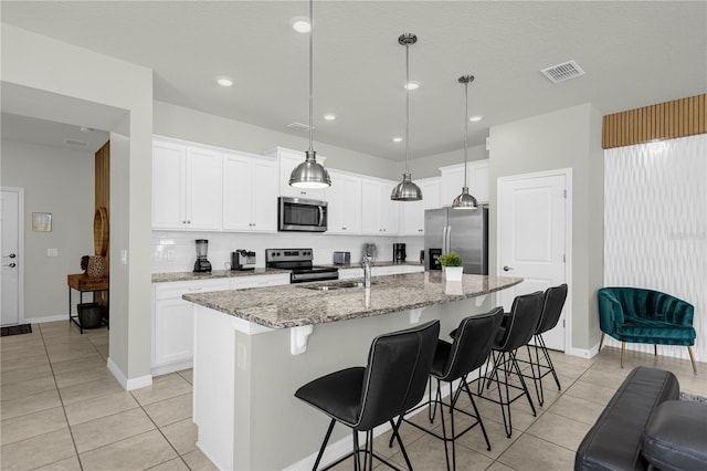 kitchen featuring white cabinets, decorative light fixtures, stainless steel appliances, and a center island with sink