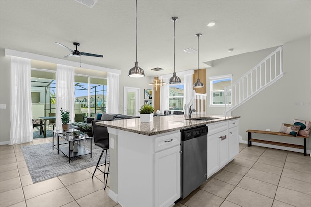 kitchen featuring light stone countertops, white cabinets, a kitchen island with sink, decorative light fixtures, and dishwasher