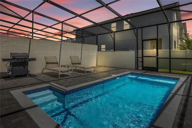 pool at dusk with area for grilling, a lanai, and a patio area