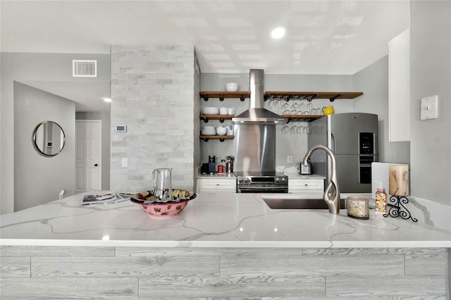 kitchen featuring sink, light stone counters, kitchen peninsula, exhaust hood, and appliances with stainless steel finishes