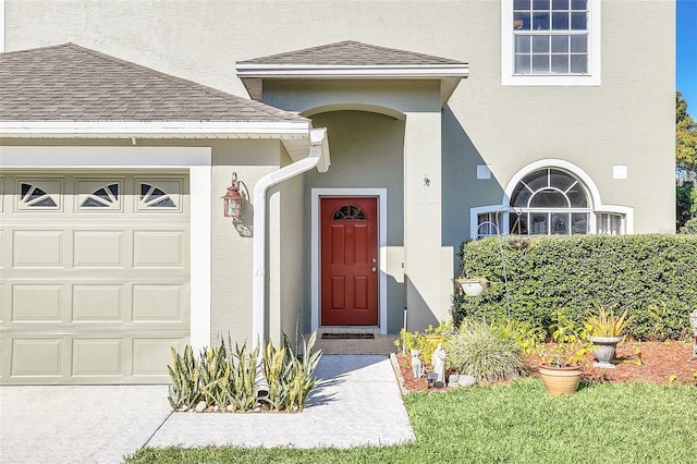 doorway to property with roof with shingles, an attached garage, and stucco siding