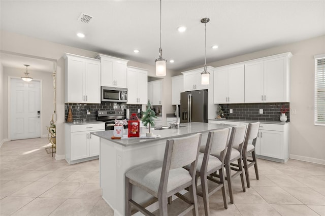 kitchen featuring white cabinets, stainless steel appliances, hanging light fixtures, and a kitchen island with sink