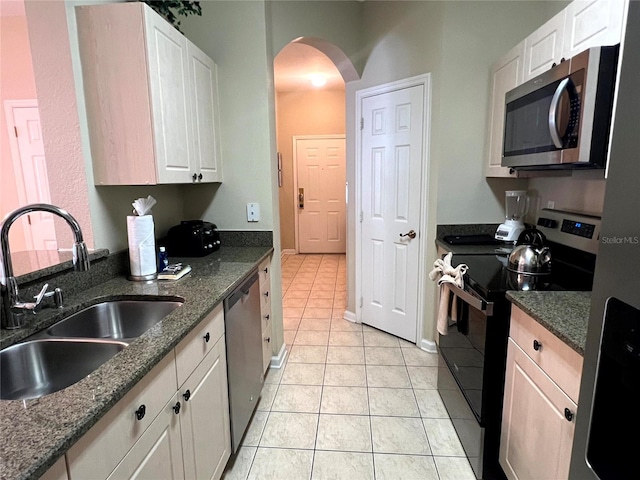 kitchen with dark stone counters, stainless steel appliances, sink, white cabinets, and light tile patterned flooring