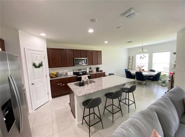 kitchen with a center island with sink, sink, a breakfast bar area, light stone counters, and stainless steel appliances