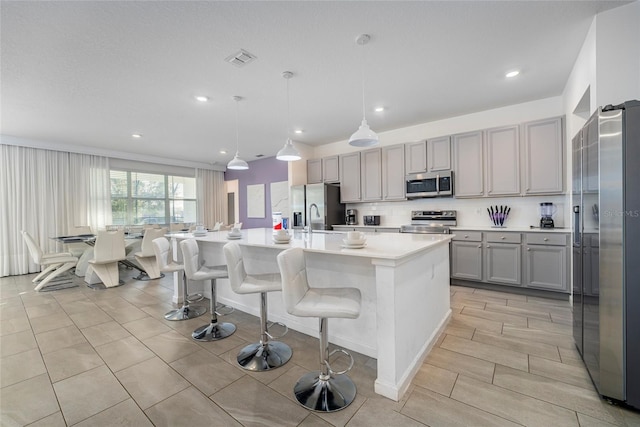 kitchen with hanging light fixtures, appliances with stainless steel finishes, gray cabinets, and a kitchen island with sink