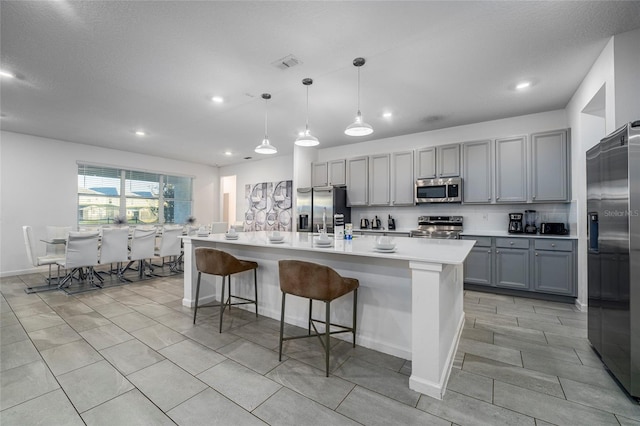 kitchen featuring gray cabinetry, stainless steel appliances, decorative light fixtures, a breakfast bar area, and an island with sink