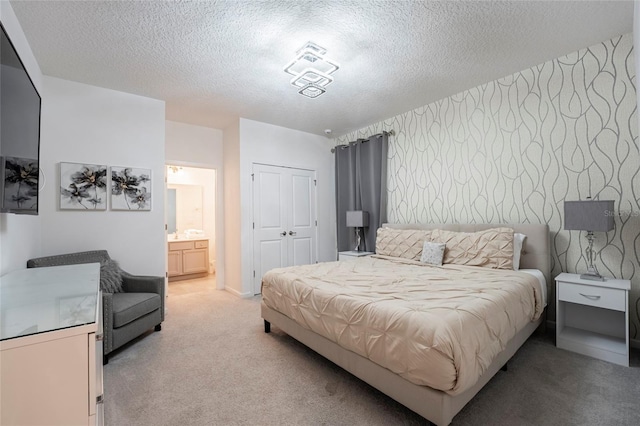 bedroom with light carpet, a textured ceiling, ensuite bathroom, and a closet