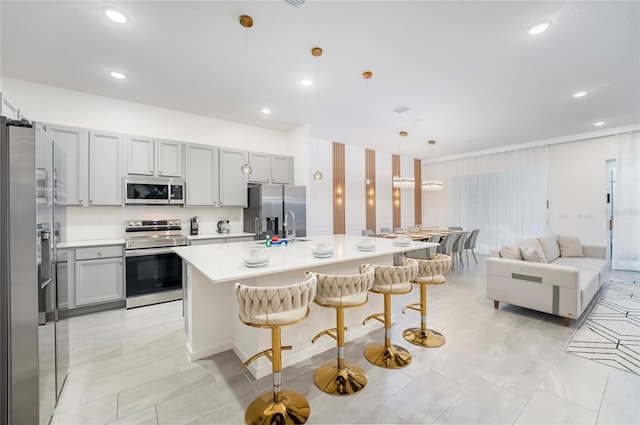 kitchen featuring a breakfast bar, decorative light fixtures, stainless steel appliances, and a kitchen island with sink