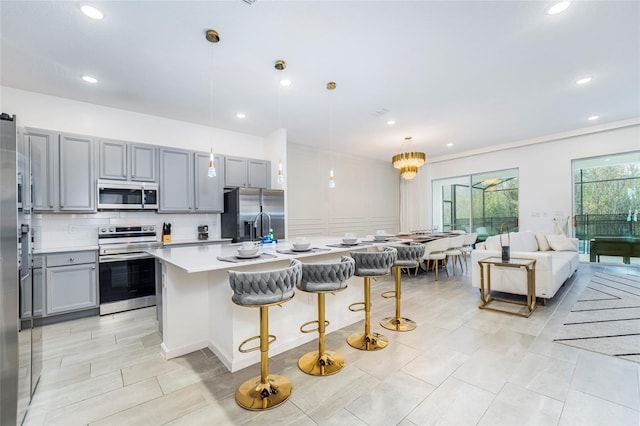 kitchen featuring stainless steel appliances, backsplash, pendant lighting, a kitchen bar, and a center island with sink