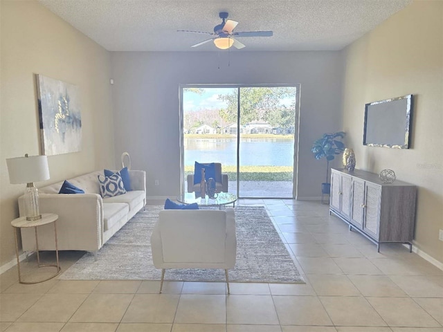 tiled living room with ceiling fan, a water view, and a textured ceiling