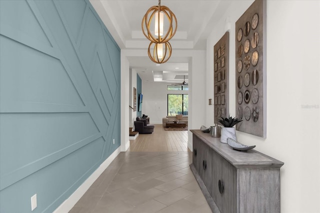 hall featuring a raised ceiling, light tile patterned floors, and an inviting chandelier