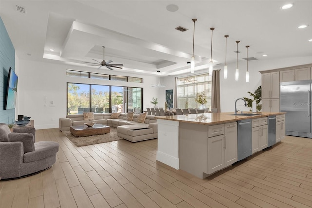 kitchen with stainless steel built in refrigerator, a tray ceiling, a kitchen island with sink, ceiling fan, and sink