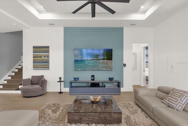 living room featuring light hardwood / wood-style flooring, a raised ceiling, and ceiling fan