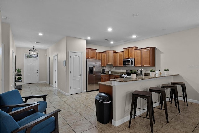 kitchen with light tile patterned flooring, kitchen peninsula, a breakfast bar area, dark stone counters, and appliances with stainless steel finishes