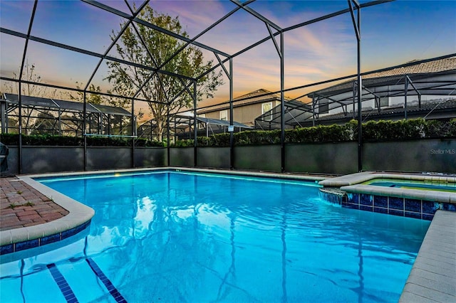 pool at dusk with glass enclosure, an in ground hot tub, and a water view