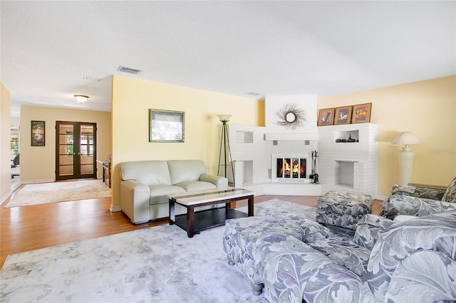 living room featuring french doors, light hardwood / wood-style floors, a brick fireplace, and a textured ceiling