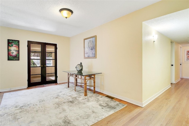 hallway with a textured ceiling, light hardwood / wood-style floors, and french doors