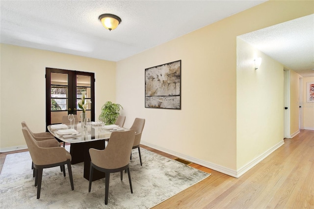 dining area featuring light hardwood / wood-style flooring, french doors, and a textured ceiling