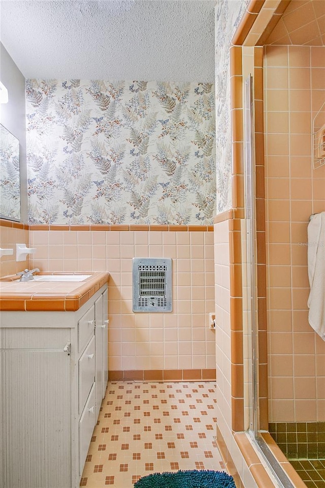 bathroom featuring heating unit, a shower with shower door, tile walls, vanity, and a textured ceiling