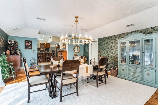 dining area featuring a textured ceiling, light hardwood / wood-style flooring, vaulted ceiling, and a notable chandelier