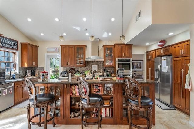 kitchen with an island with sink, stainless steel appliances, a breakfast bar area, and wall chimney range hood