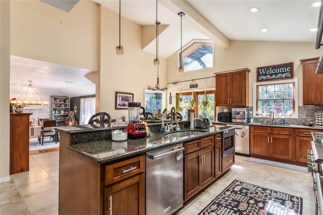 kitchen with appliances with stainless steel finishes, dark stone counters, sink, a kitchen island, and hanging light fixtures