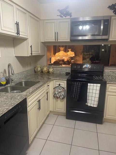 kitchen featuring black appliances, sink, light tile patterned floors, cream cabinetry, and light stone counters