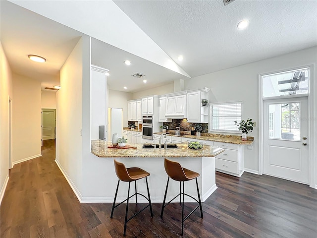 kitchen with white cabinetry, sink, light stone counters, dark hardwood / wood-style floors, and kitchen peninsula