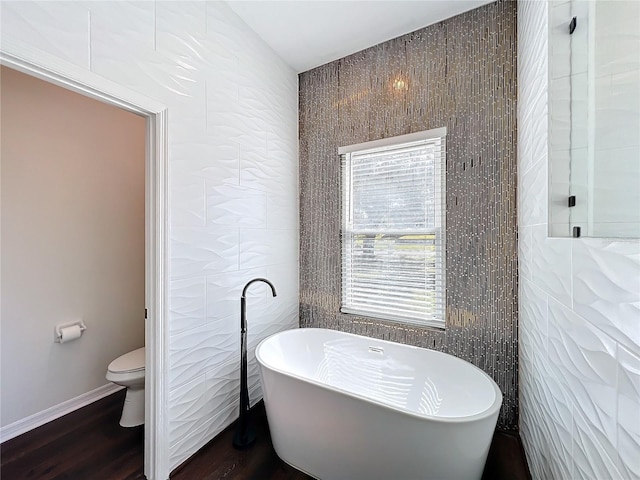 bathroom with a bathing tub, toilet, hardwood / wood-style floors, and tile walls