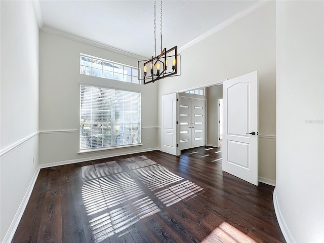 unfurnished dining area with a high ceiling, a chandelier, dark hardwood / wood-style floors, and ornamental molding