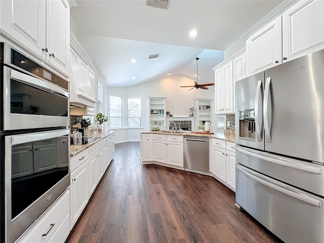 kitchen featuring stainless steel appliances, light stone counters, kitchen peninsula, vaulted ceiling, and white cabinets