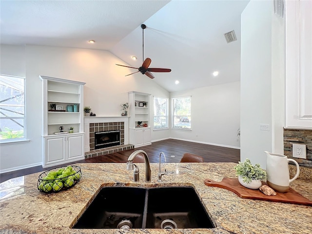 kitchen featuring a tile fireplace, sink, vaulted ceiling, ceiling fan, and light stone counters