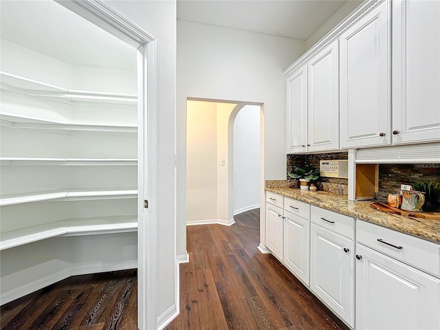 bar featuring backsplash, light stone counters, white cabinets, and dark hardwood / wood-style floors