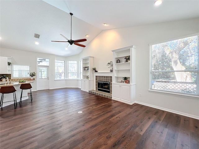 living room featuring dark hardwood / wood-style flooring, ceiling fan, sink, a tile fireplace, and lofted ceiling