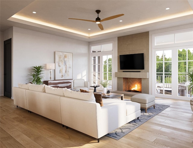 living room with ceiling fan, a raised ceiling, light wood-type flooring, and a tiled fireplace