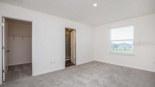 unfurnished bedroom with a closet, light colored carpet, a spacious closet, and ensuite bath