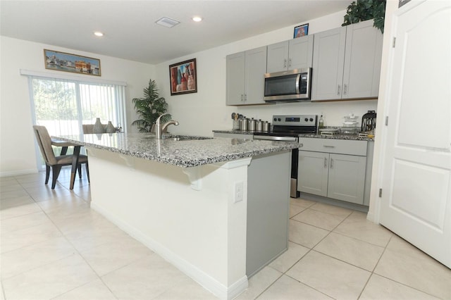 kitchen with appliances with stainless steel finishes, gray cabinetry, and an island with sink