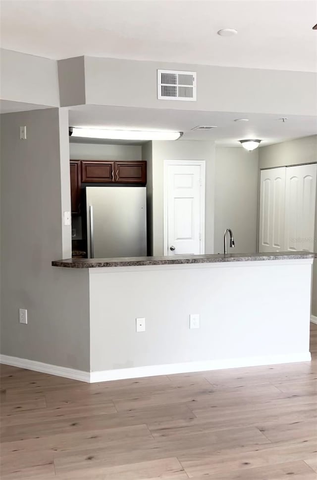 kitchen featuring kitchen peninsula, light hardwood / wood-style flooring, and fridge