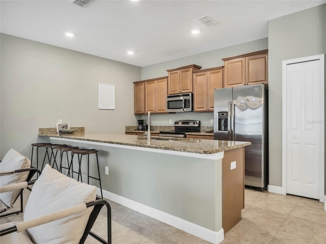 kitchen with light stone countertops, kitchen peninsula, stainless steel appliances, light tile patterned floors, and a breakfast bar area