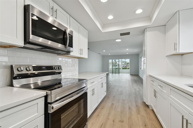 kitchen with white cabinets, light wood-type flooring, appliances with stainless steel finishes, and tasteful backsplash