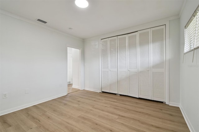 unfurnished bedroom with light wood-type flooring, ornamental molding, and a closet