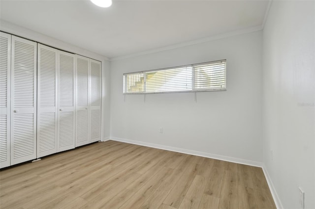 unfurnished bedroom with light wood-type flooring, crown molding, and a closet