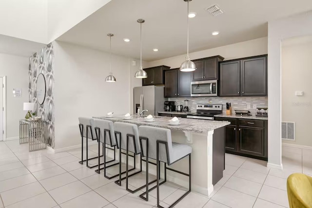 kitchen featuring dark brown cabinetry, hanging light fixtures, an island with sink, and stainless steel appliances