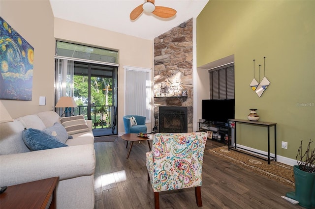 living room featuring ceiling fan, dark hardwood / wood-style flooring, vaulted ceiling, and a stone fireplace