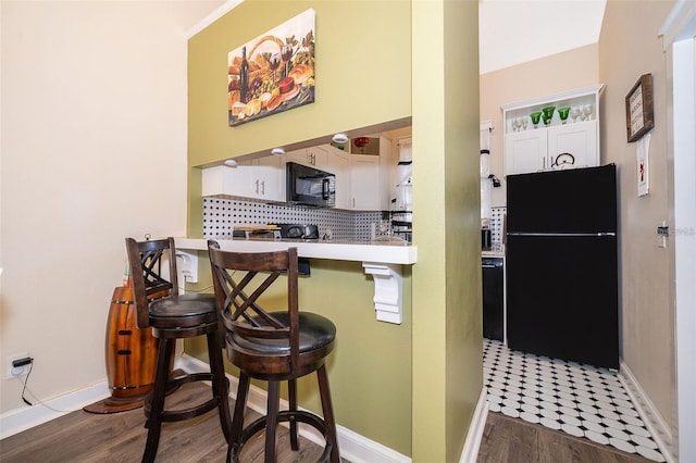 kitchen with dark wood-type flooring, black appliances, a kitchen breakfast bar, kitchen peninsula, and white cabinets