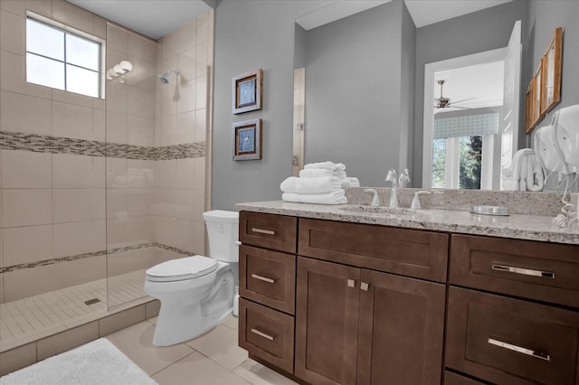 bathroom with a tile shower, vanity, ceiling fan, tile patterned flooring, and toilet