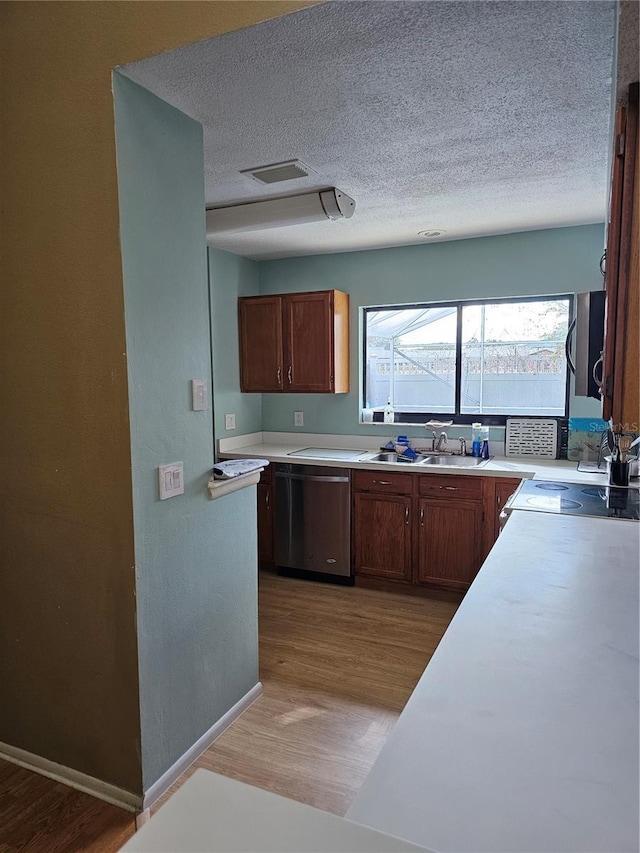 kitchen featuring a textured ceiling, light hardwood / wood-style floors, stainless steel dishwasher, and sink