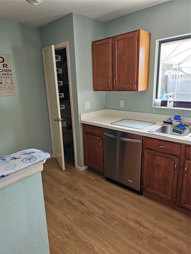 kitchen with a textured ceiling, light hardwood / wood-style flooring, stainless steel dishwasher, and sink