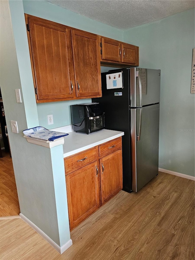 kitchen featuring stainless steel refrigerator, light hardwood / wood-style floors, and a textured ceiling