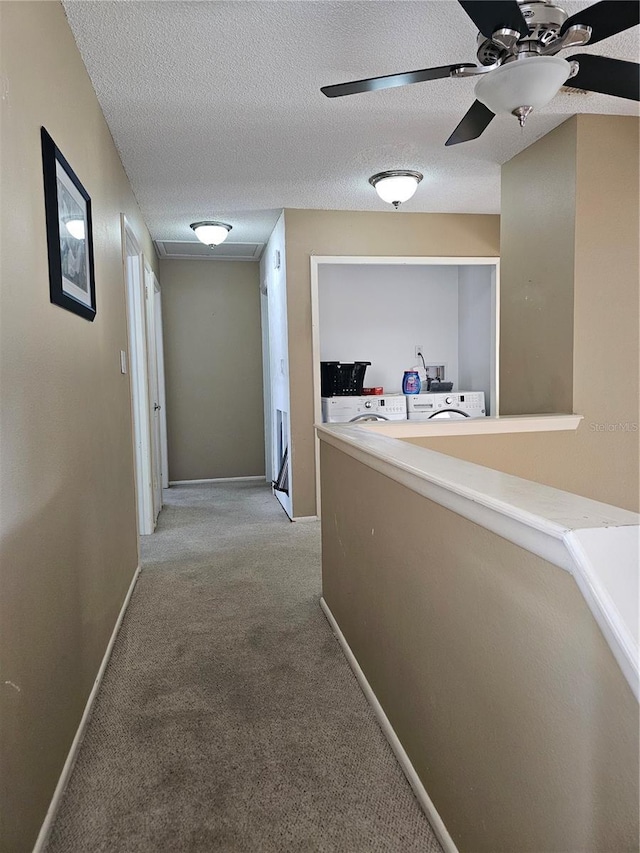 corridor with light colored carpet, a textured ceiling, and independent washer and dryer